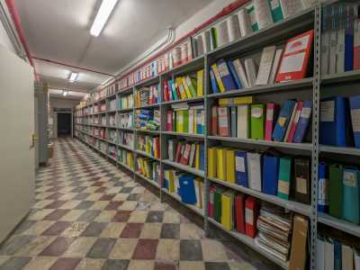 Una porta in metallo d� accesso invece a un lungo corridoio: le pareti dell�ambiente, e dei vani adiacenti, sono interamente occupate da lunghi scaffali con centinaia di faldoni